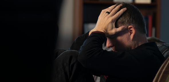 A man sitting on a couch holding his head in his hands